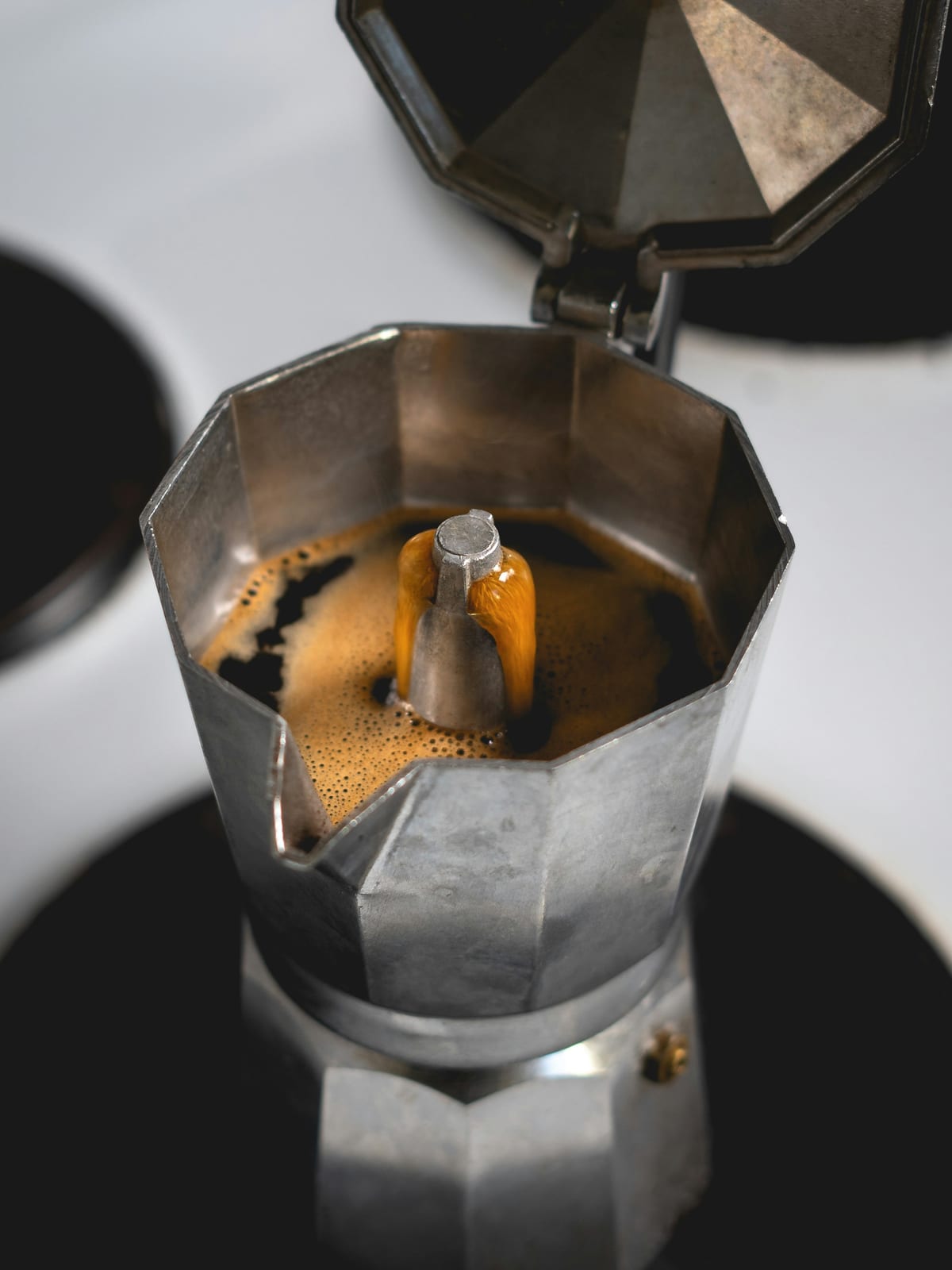An open moka pot on a hob, freshly brewed coffee welling up around the spout in the upper chamber