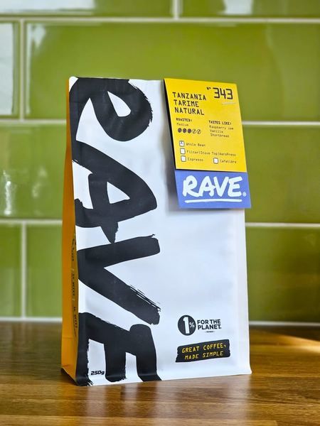 A 250g bag of Rave Coffee standing on a wooden worktop against green tiles, its label reading Tanzania Tarime Natural