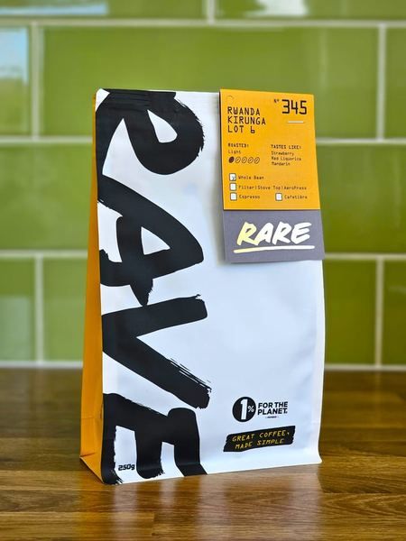 A 250g bag of Rave Coffee from the Rare range standing on a wooden worktop against green tiles, its label reading Rwanda Kirunga Lot 6