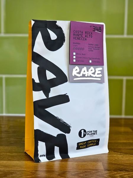 A 250g bag of Rave Coffee from the Rare range standing on a wooden worktop against green tiles, its label reading Costa Rica Monte Alto Venecia