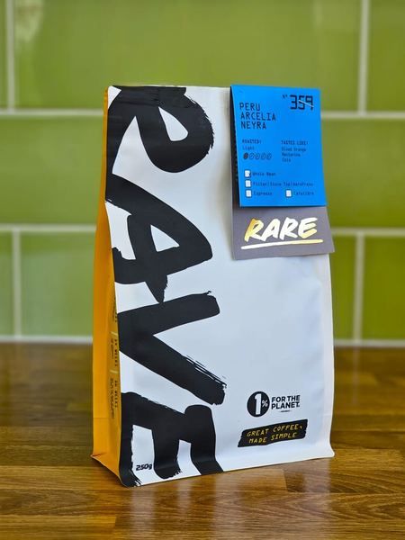 A 250g bag of Rave Coffee from the Rare range standing on a wooden worktop against green tiles, its label reading Peru Arcelia Neyra